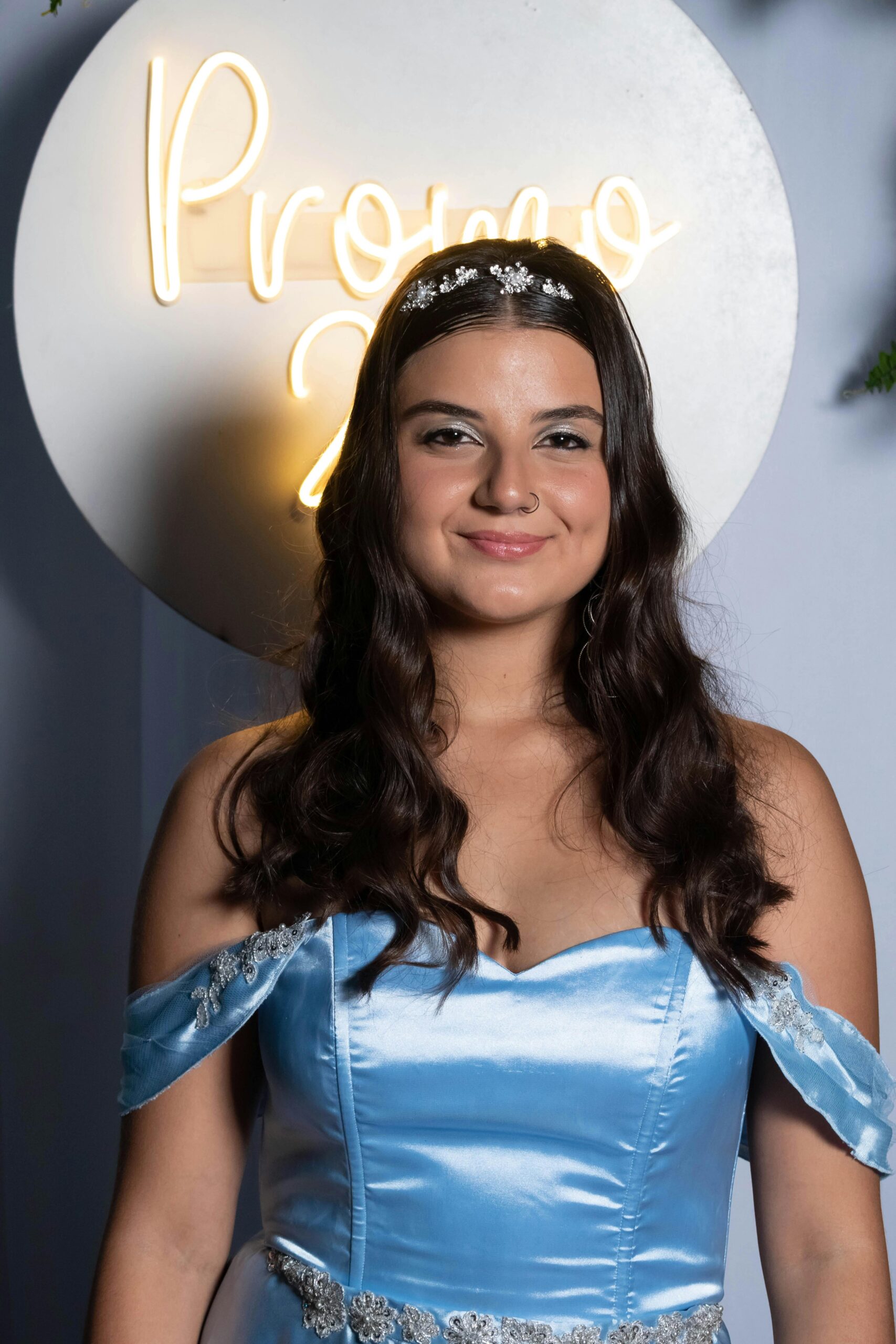 Young woman in satin dress smiling at prom night with glowing backdrop.